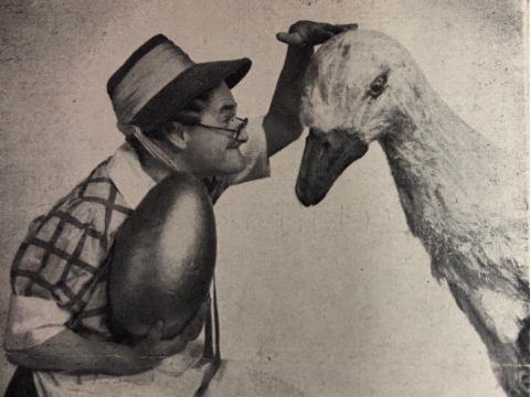 Black and white photograph of pantomime dame Norman Evans petting a toy goose and holding a giant egg.
